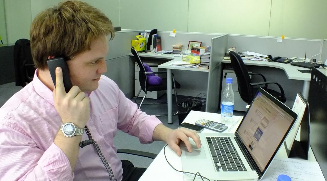 Male Projects Abroad Business Intern is on the phone in a marketing office during his Business Work Experience in China. Male business intern sits at a desk on the phone in a marketing office during his internship in China.